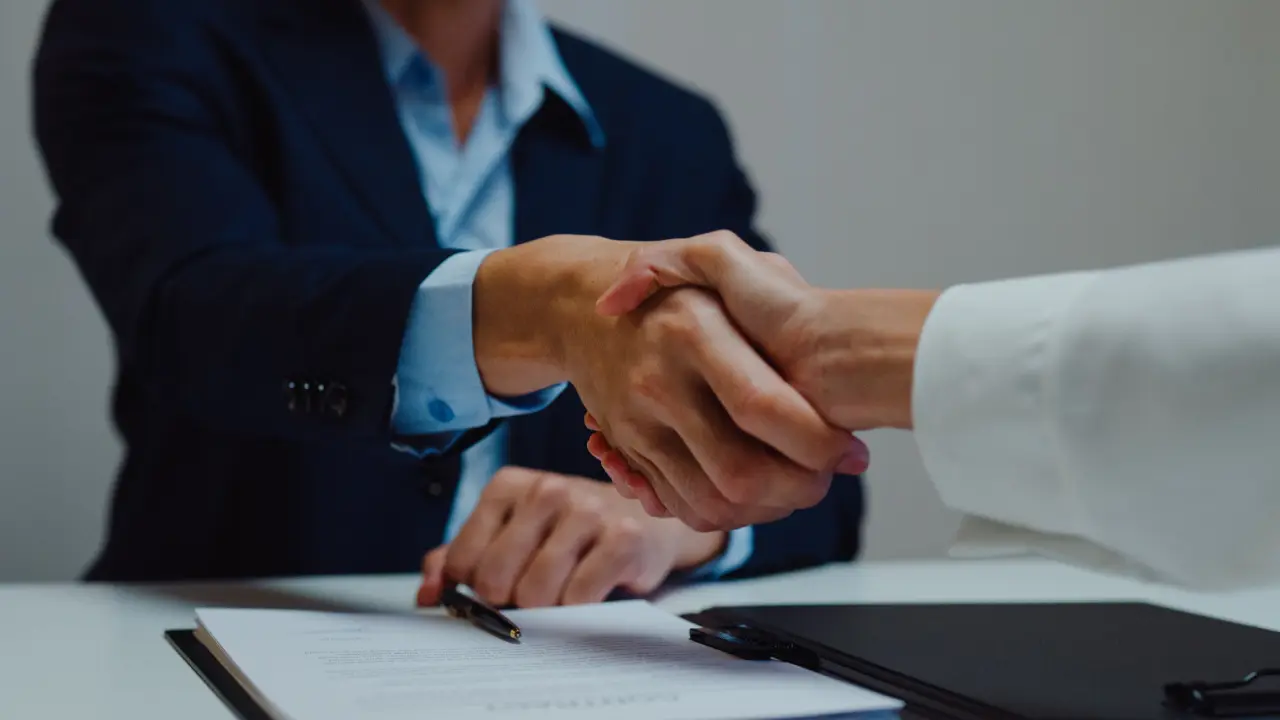 Two people shaking hands over a table.